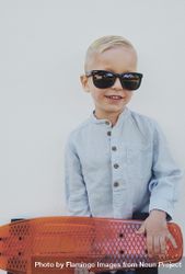 Young trendy blond boy leaning against a wall with red skateboard, vertical 5kAzAb