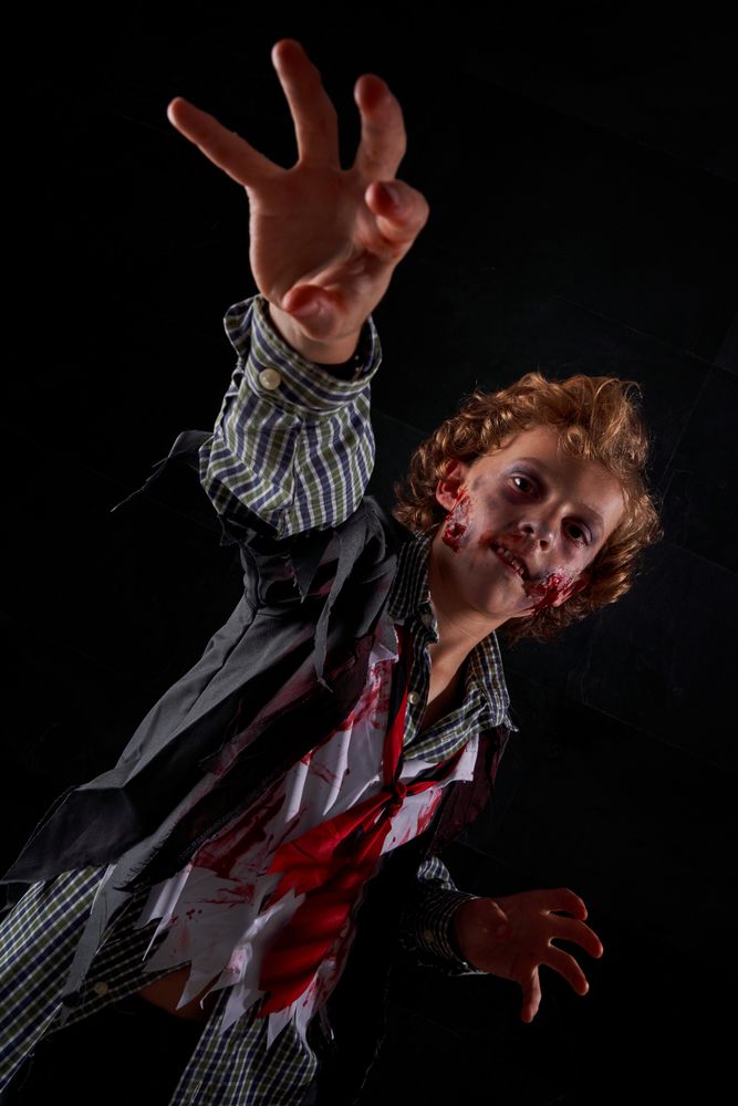 Vertical photo of a boy disguised as a zombie with blood with his arms raised trying to catch something in front of him