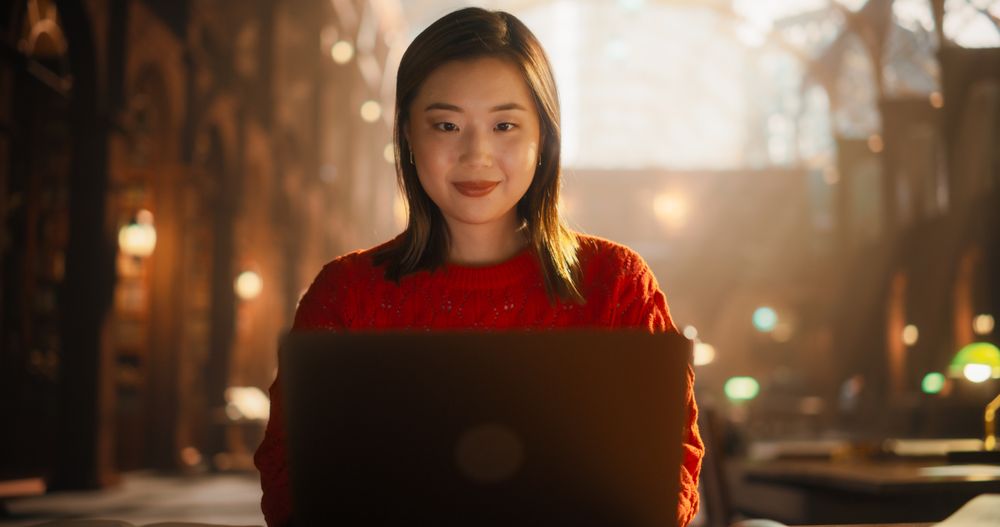 Engaged Asian Female Student Studying With Laptop in Historic Library