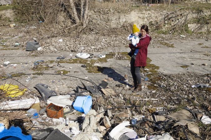 Woman holding her baby in rubble and garbage
