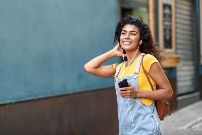 Arab woman listening to music with earphones and walking through quiet street