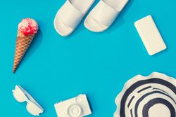 Summer objects of flip flops, sunglasses, camera, smart phone, hat and ice cream on blue background