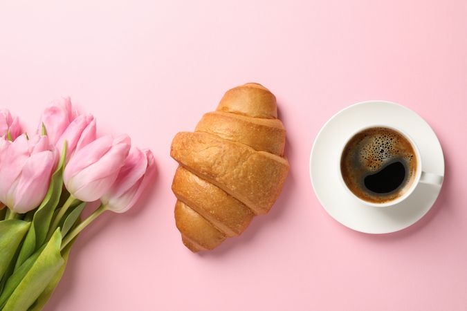 Tulips, croissant and cup of coffee on pink background, top view