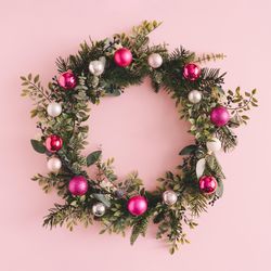 Christmas wreath made of decorative baubles and branches on pink background