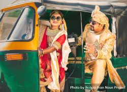 Indian bride and groom in traditional wedding outfit sitting in tuk-tuk 0vraZ0