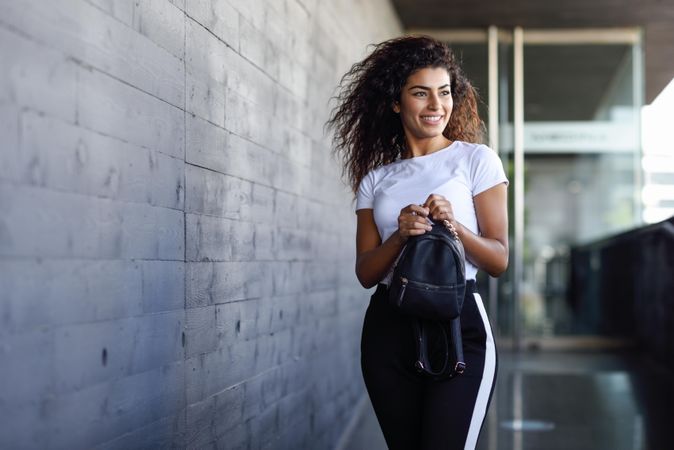 Happy Arab woman walking out of building with bag, copy space