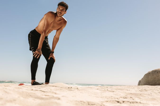 Fit male bending down to his knees after workout on a beach