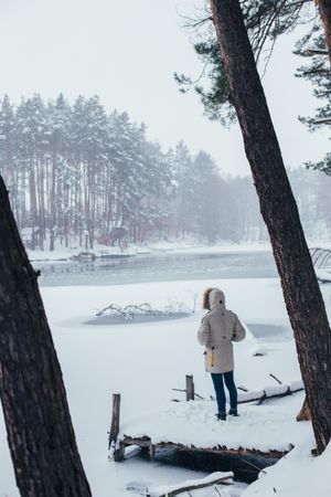 Man in parka outside looking out onto lake in snowy forest