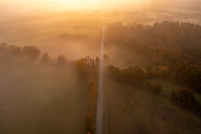 Drone aerial image with an autumn forest and a road on a foggy morning at golden hour