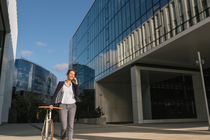 Cheerful manager with bicycle talking on smartphone