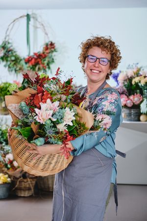 Smiling woman with bouquet of flowers in basket in floral store