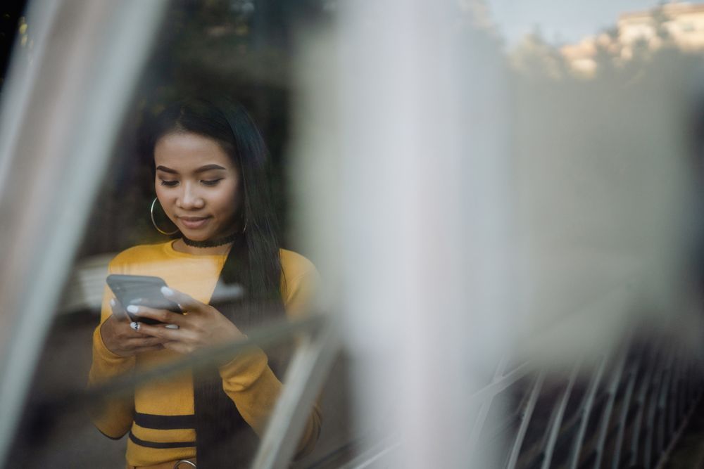 Charming Asian woman browsing smartphone through glass window