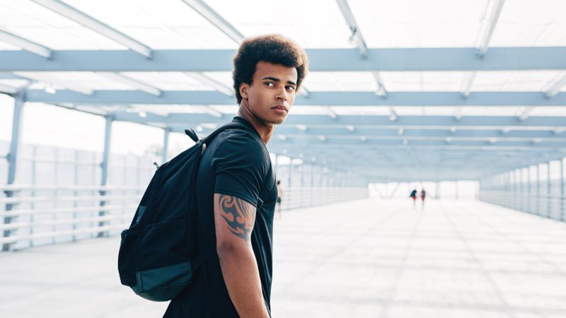 Young Black man walking along bridge with backpack