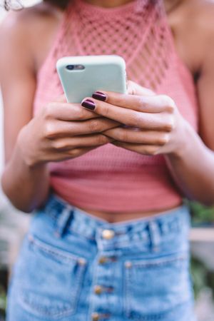 Young woman’s manicured hands holding a mobile phone and texting