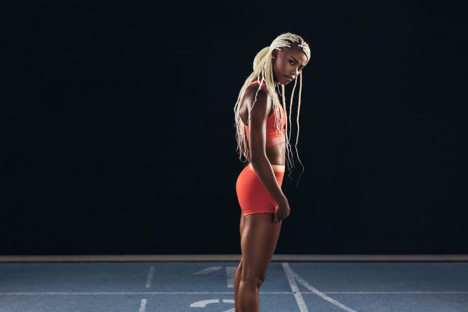 Female sprinter standing at the start line on a running track on a dark background