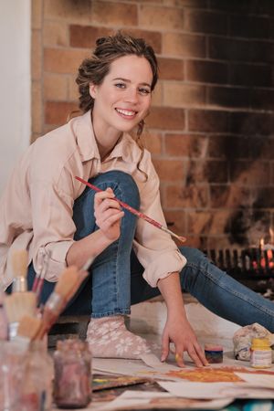 Cheerful woman with brush painting on floor at home