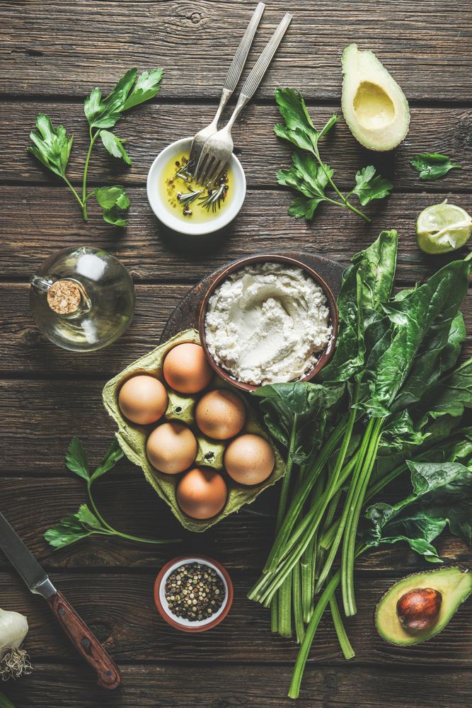 Preparing spinach ricotta stuffing with herbs, eggs and spices at dark wooden kitchen table. Cooking at home with fresh healthy ingredients. Top view.
