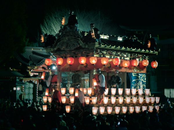 Japanese style structure decorate with light lanterns surrounded by people at nighttime