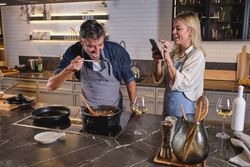 Happy multiethnic couple cooking and taking photo in kitchen