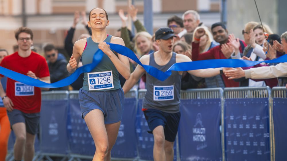 Portrait of Athletic Female Jogger Crossing the Finish Line in Marathon Race with the Audience Cheering.
