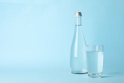 Water bottle with glass full of water in light blue space