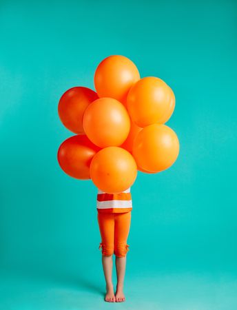 Girl holding orange balloons in front on blue background