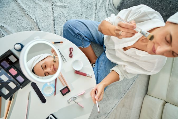 Relaxed woman applying facial cream with brush on face