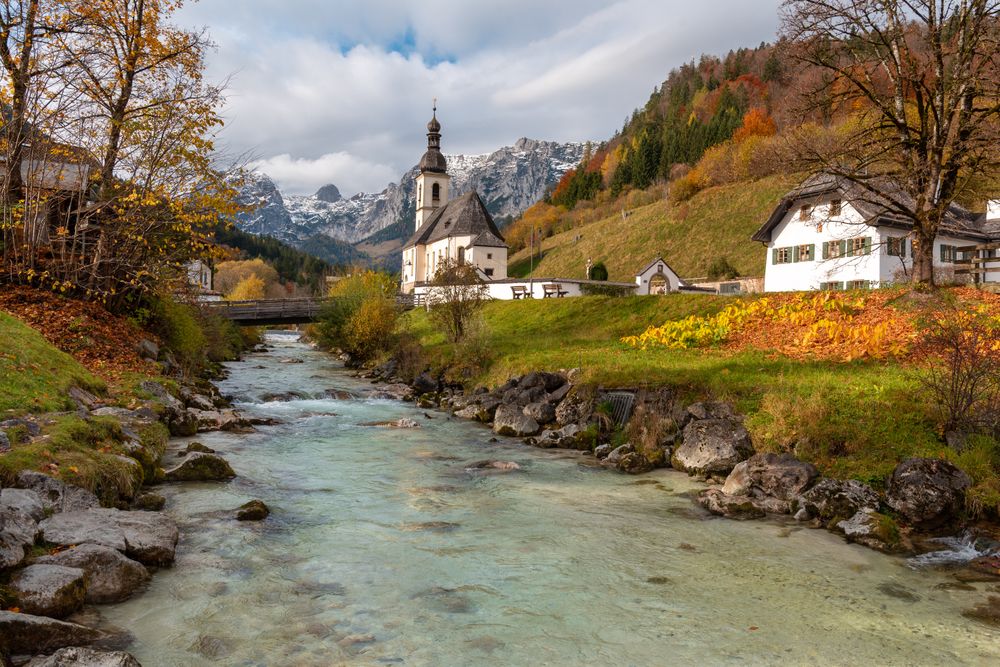 Autumn landscape with church on river bank surrounded by mountains