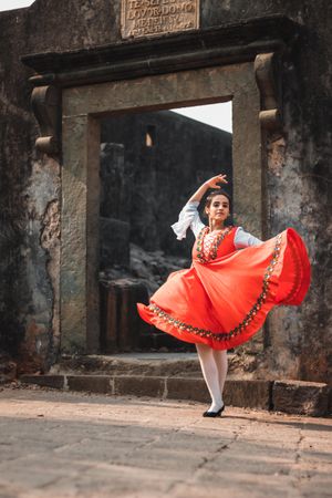 Woman in red traditional dress dancing in front of stone gate