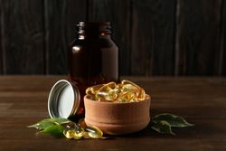 Wooden bowl with omega pills on dark background