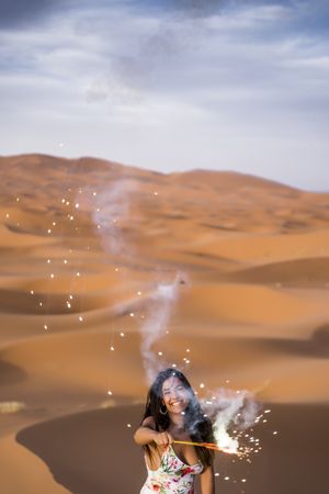 Happy woman holding firework in desert