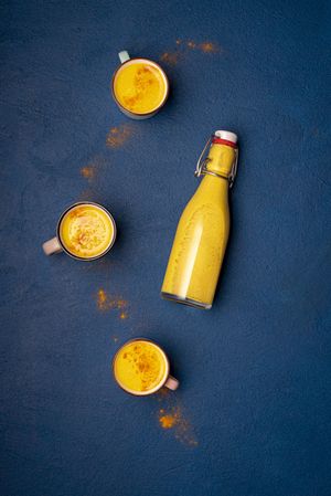 Turmeric latte in bottle and cups with extra spice powder sprinkled around