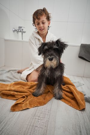 Boy in robe stroking wet fluffy dog after bath