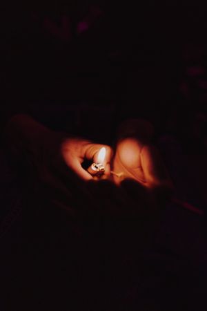 Hands holding up a lighter to a marijuana joint in darkness