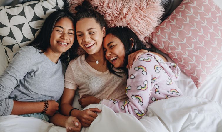 Group of girls laughing and having fun while lying on bed together during sleepover