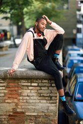Calm male sitting with one leg up on brick wall in city with eyes closed