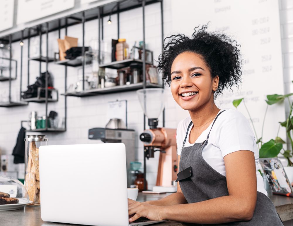 Smiling small business owner working on laptop in her cafe 