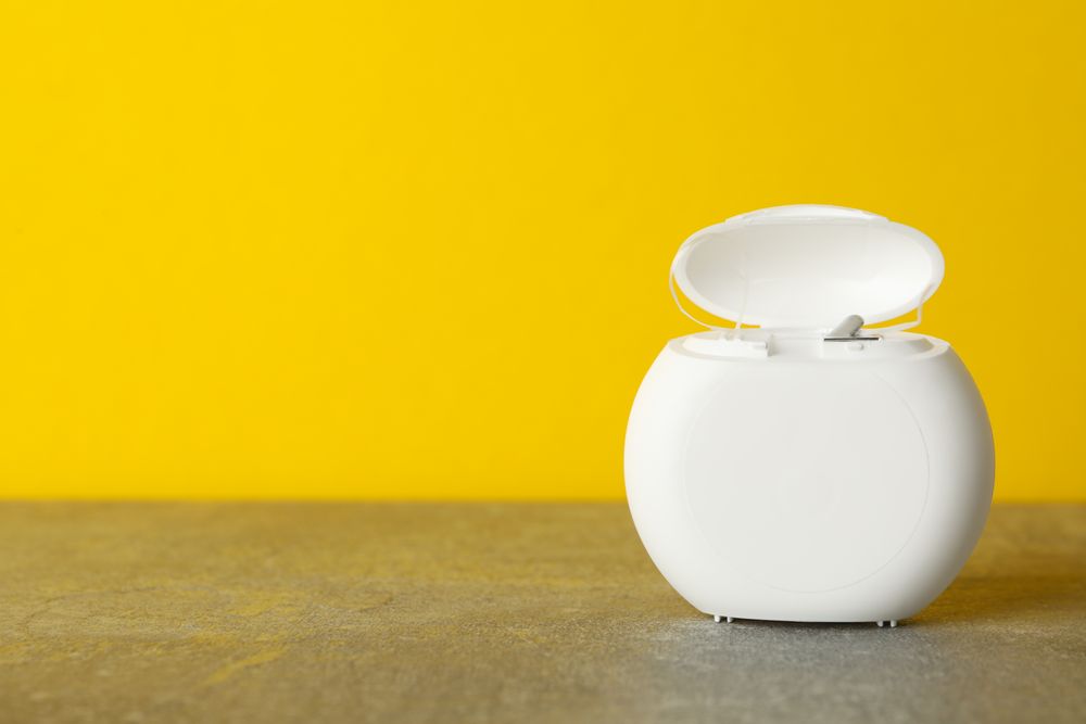 Tooth floss on gray table against yellow background, space for text