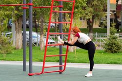 Woman stretching leg on outdoor fitness equipment in park.