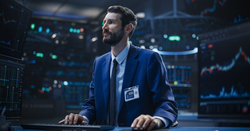 Adult Stock Exchange Broker Working on a Desktop Computer with Real-Time Stock Information, Commodities and Exchange Market Charts.
