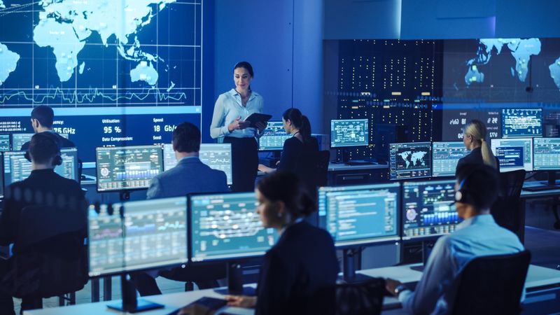 Supervisor Briefs Team in High-tech Operations Center. Analysts Monitor Global Data on Multiple Screens.