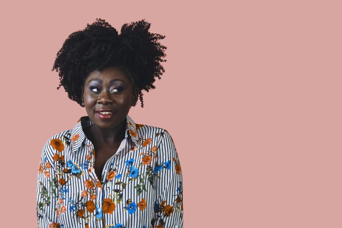 Studio shot of curious Black woman in floral print shirt looking to the side