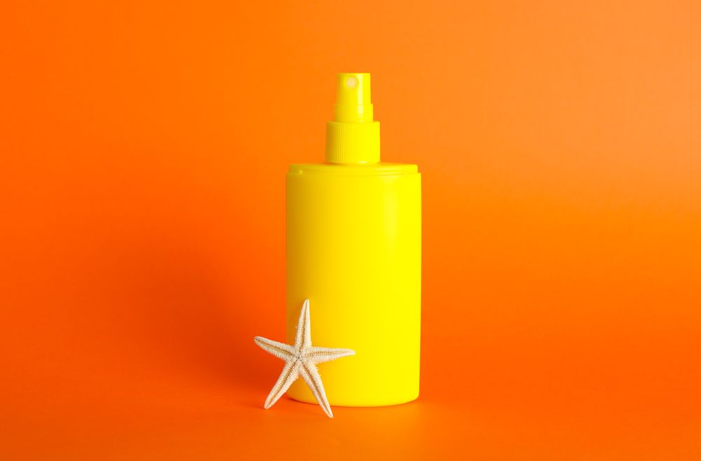 Sunscreen spray with starfish on color background, space for text
