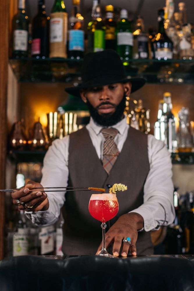 stylish Black bartender offering a customer a cocktail decorated with garnish in a traditional cocktail bar