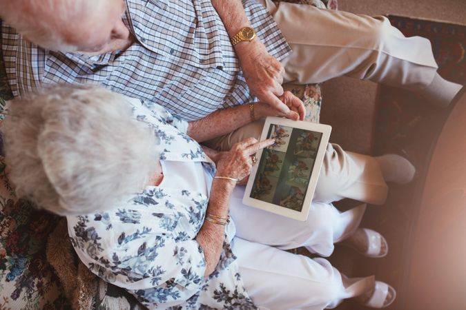 Top view of older couple sitting together looking at pictures on digital tablet