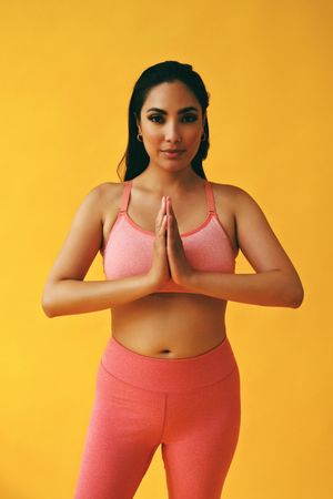Hispanic woman in yoga clothes with hands together looking at camera