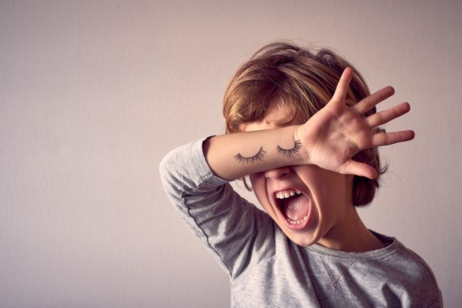 Annoyed boy covering eyes with hand with painted eyelashes