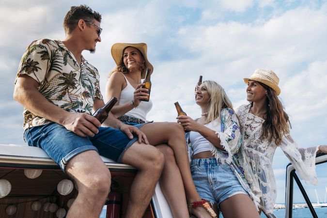Smiling friends clinking bottles celebrating vacation on car roof in bright day