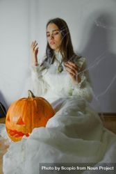 Woman in light dress sitting beside pumpkin indoor 5r1e30