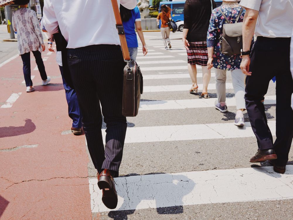 Back view of man holding suitcase walking in a busy street